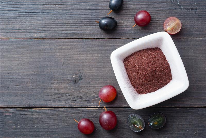 A bowl of BioVin extract sits on a wood table with full and cut grapes surrounding it.